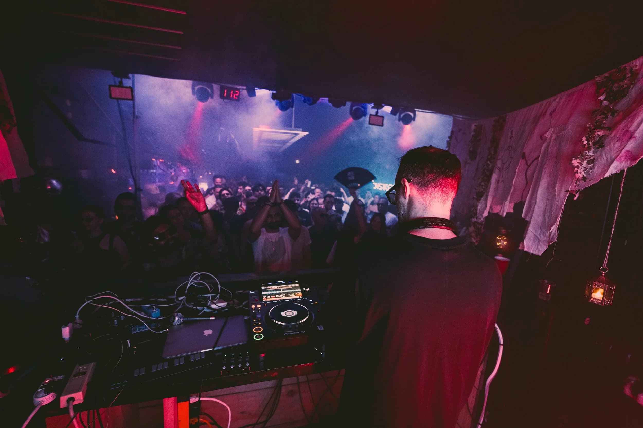 An RSN8 crowd under red light, hands in the air